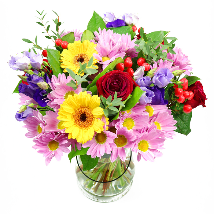 The photograph presents a generous mixed bouquet arranged in a transparent glass vase, placed against a pristine white background that highlights the vivid colours and fine details. Deep red roses form the emotional core of the design, their velvety petals spiralling outwards and giving the arrangement a rich, romantic depth. Encircling these are clusters of soft pink daisies or chrysanthemums, each bloom composed of many slender petals around a yellow disk, building a gentle, uplifting volume that softens the intensity of the roses. Two bright yellow gerbera daisies with dark brown-orange centres stand out with bold, open faces, adding a joyful, almost sun-like presence that feels naturally suited to birthday wishes or congratulatory messages in Colindale. Interwoven among the larger flowers are elegant purple and lavender lisianthus, their graceful, bell-shaped blossoms and gently ruffled edges introducing a cool sophistication and a slightly whimsical touch. Throughout the bouquet, polished red hypericum berries appear in small, rounded clusters, catching the light and offering a contemporary textural contrast to the soft petals. A varied selection of greenery anchors and frames the composition: broad, darker leaves create a strong outline, while slimmer, fresher green stems and sprigs give the impression of movement and garden freshness, as though the bouquet might have been gathered after a stroll through green spaces near Colindale. The clear glass vase reveals neatly cut stems arranged in clear water, underlining the professional finish and careful craftsmanship. Overall, the bouquet conveys a feeling of happiness, generosity, and everyday luxury, ideal as a centrepiece on a dining table, a warm welcome in a hallway, or a same-day delivery to brighten someone's day anywhere in Colindale and the surrounding neighbourhoods.